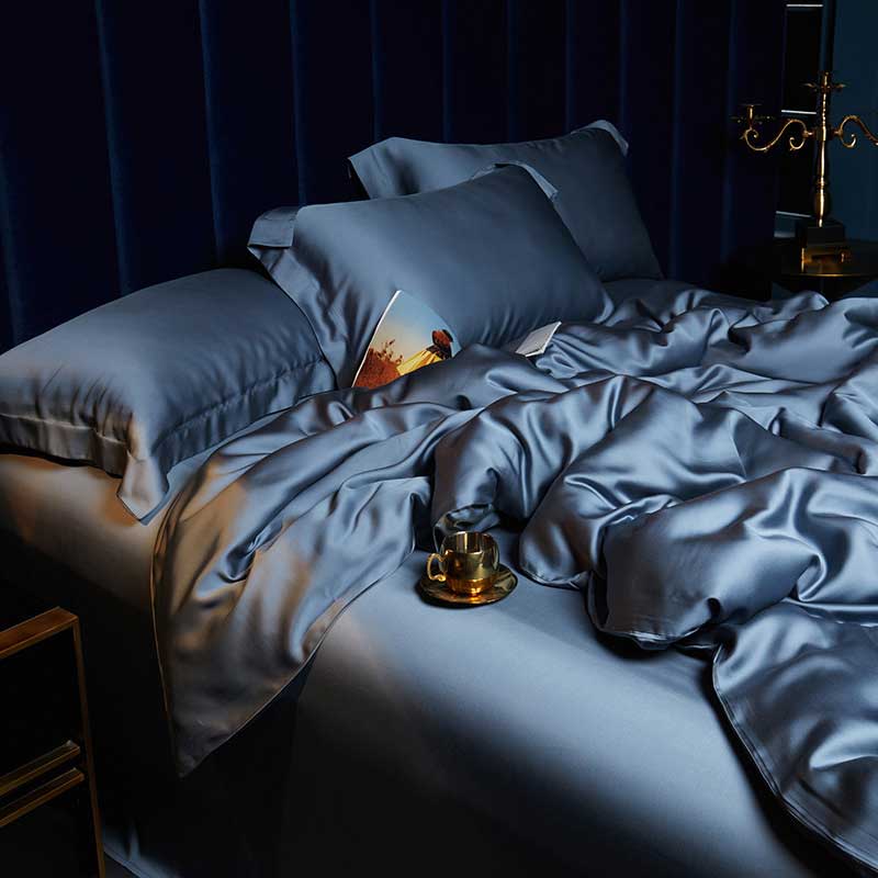 Dark blue bedding set on a bed with a candle and book in a dimly lit room.