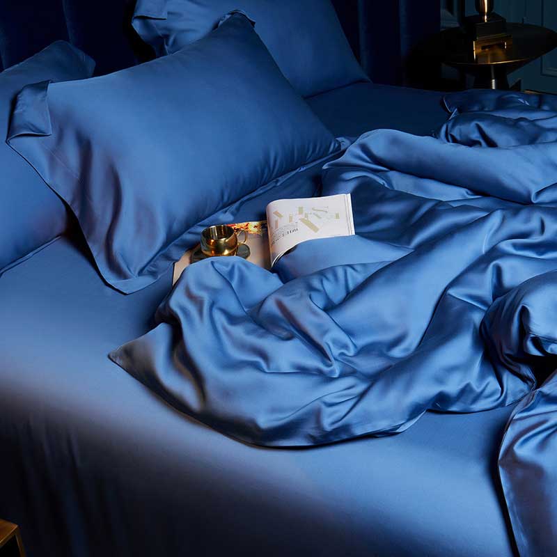 Blue bedding set on a bed with a book and small lamp in the night setting