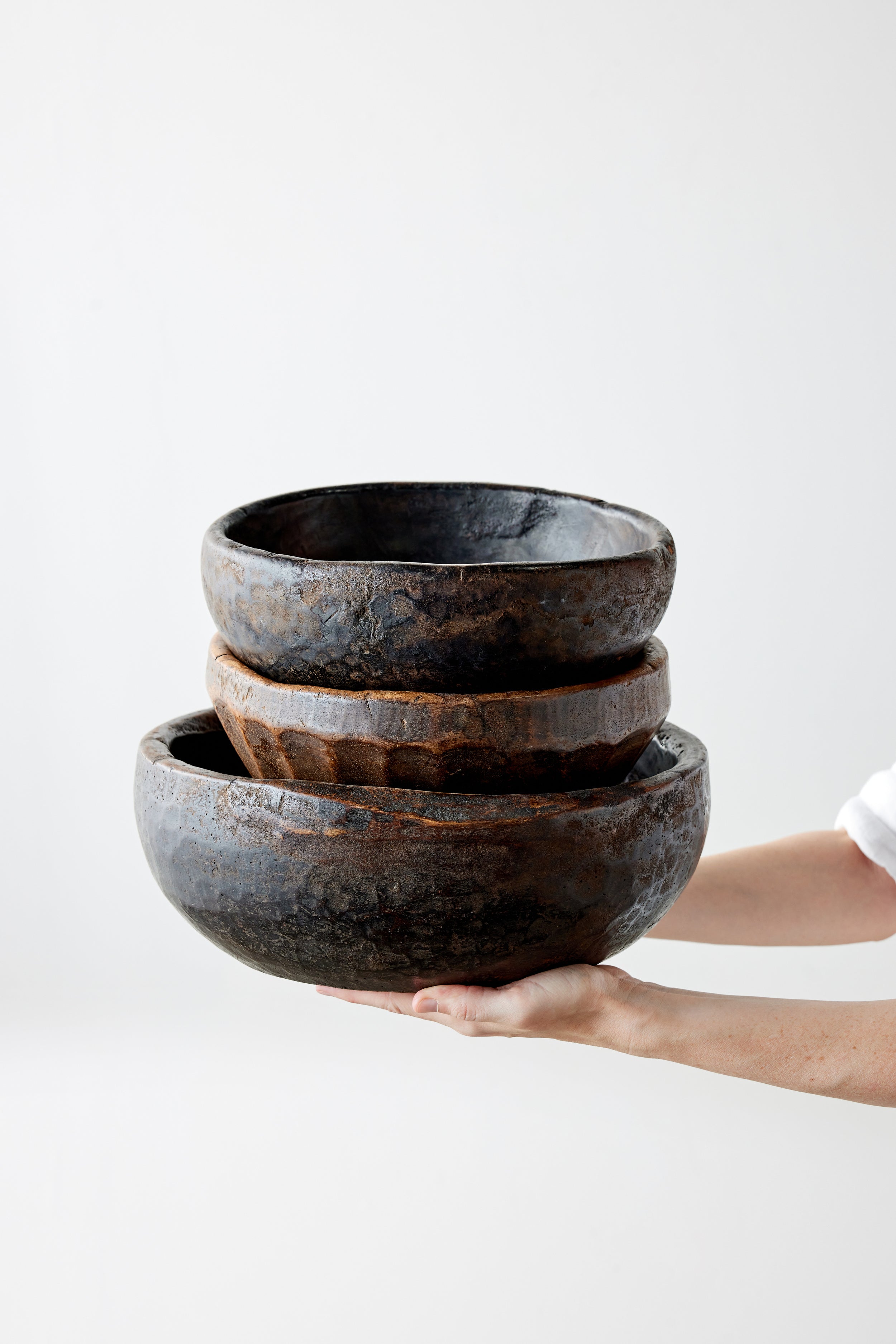 Stack of three dark brown wooden bowls held by a person on a white background