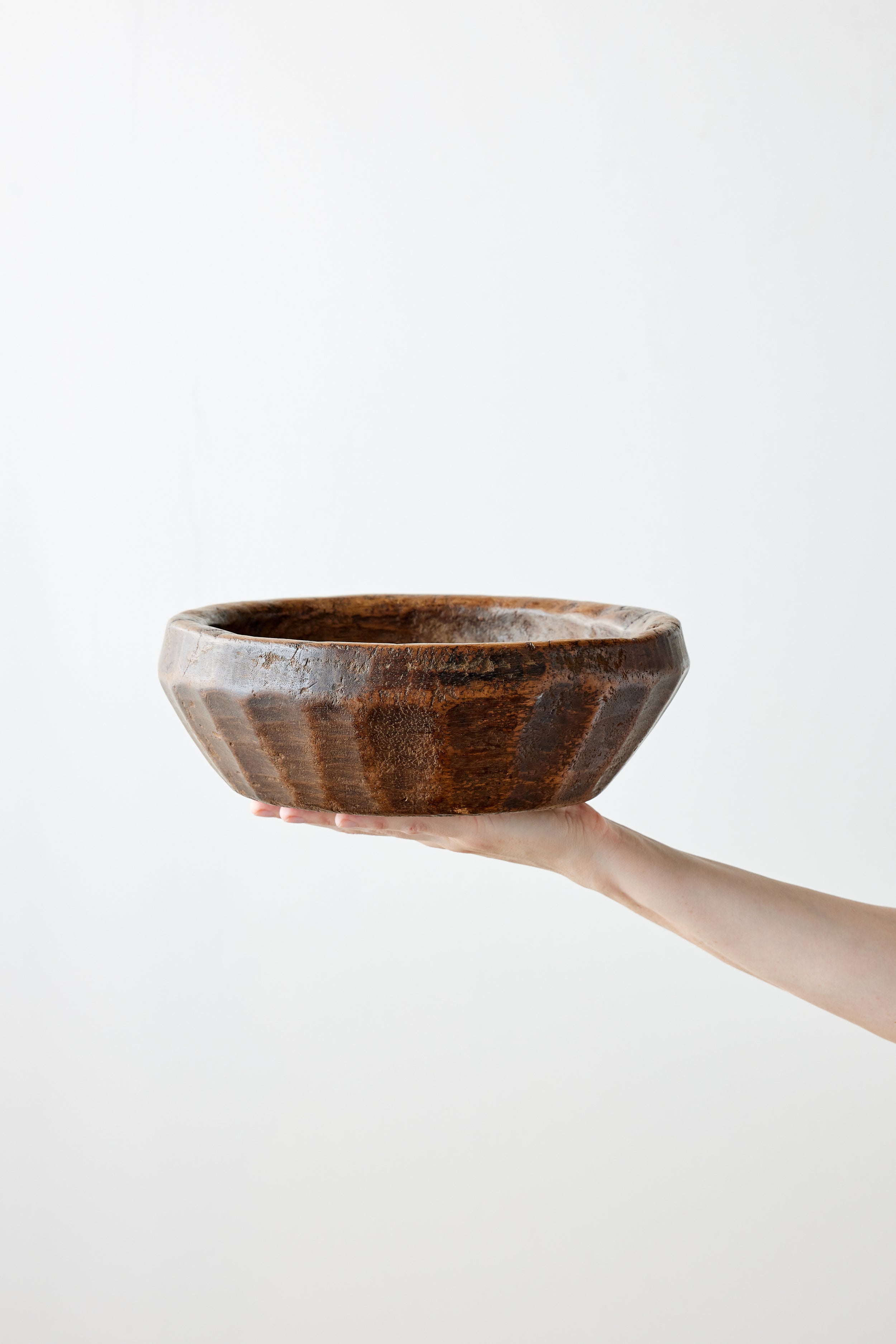 Hand holding a brown wooden bowl against a white background