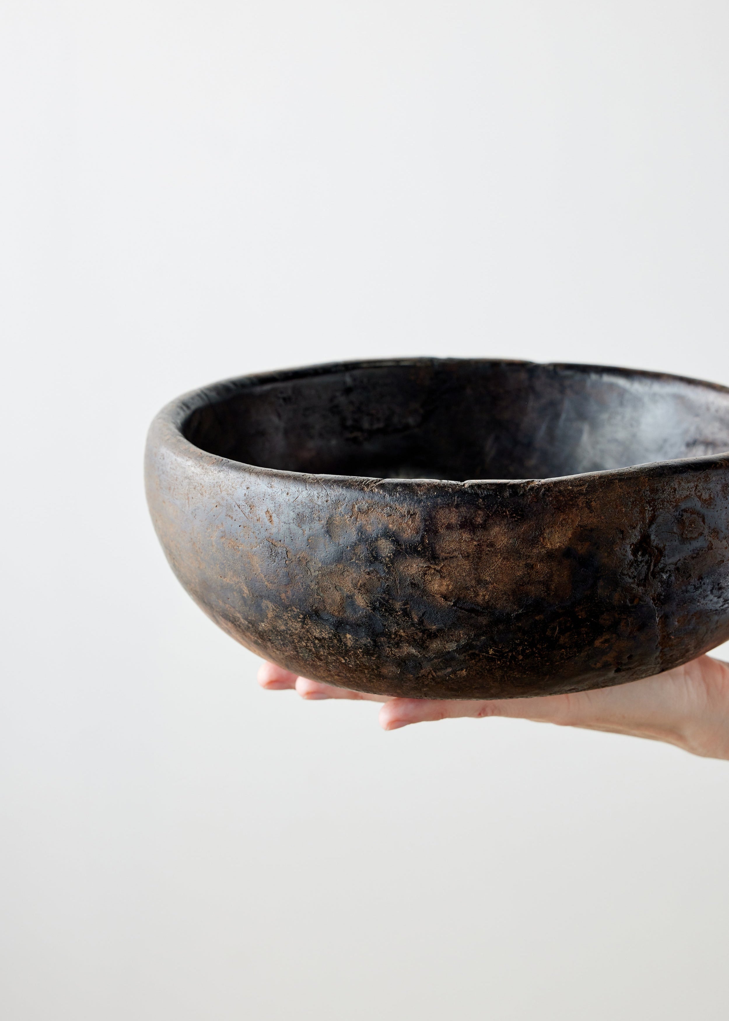Hand holding a dark brown wooden bowl against a light gray background