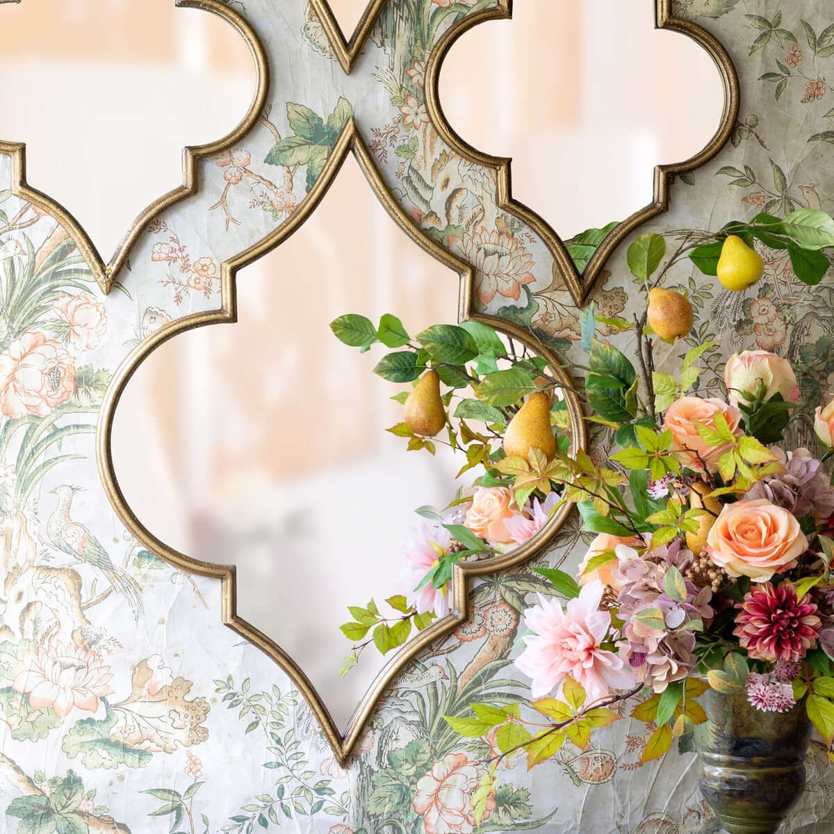Decorative wall mirrors with floral and fruit arrangement on a patterned wall.