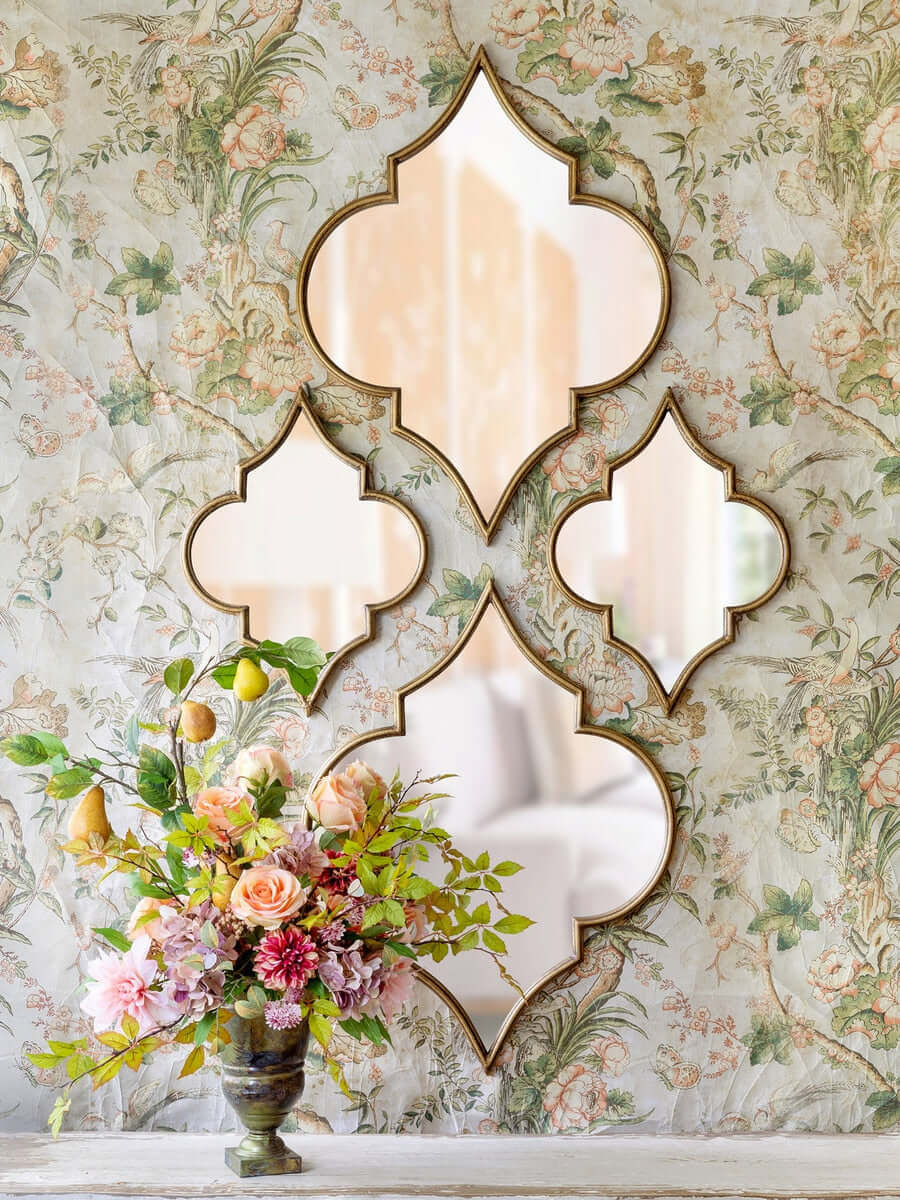 Decorative wall mirror with a floral design on a floral wallpapered wall.