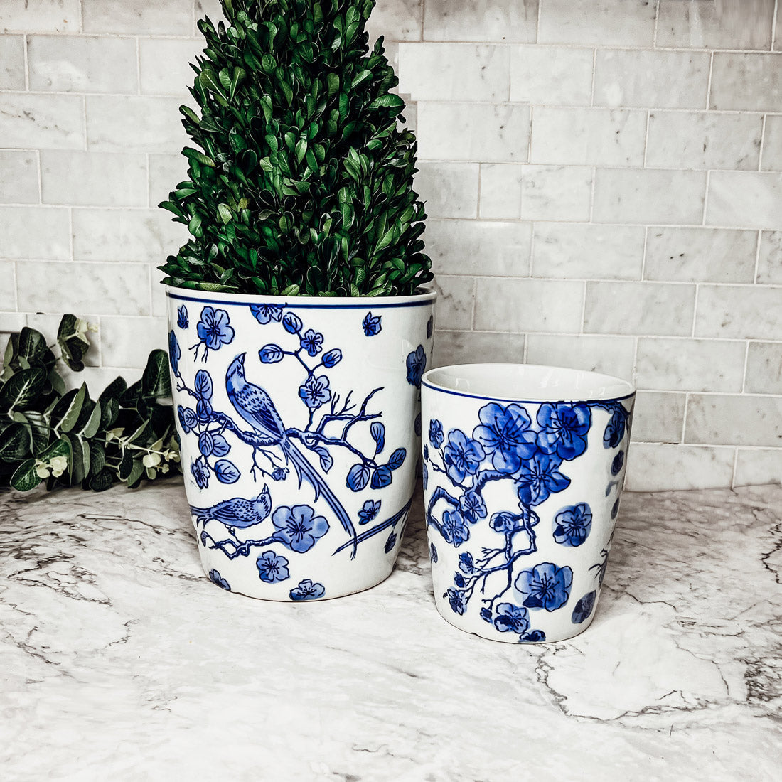 Two ceramic planters with blue floral and bird designs on a marble surface.