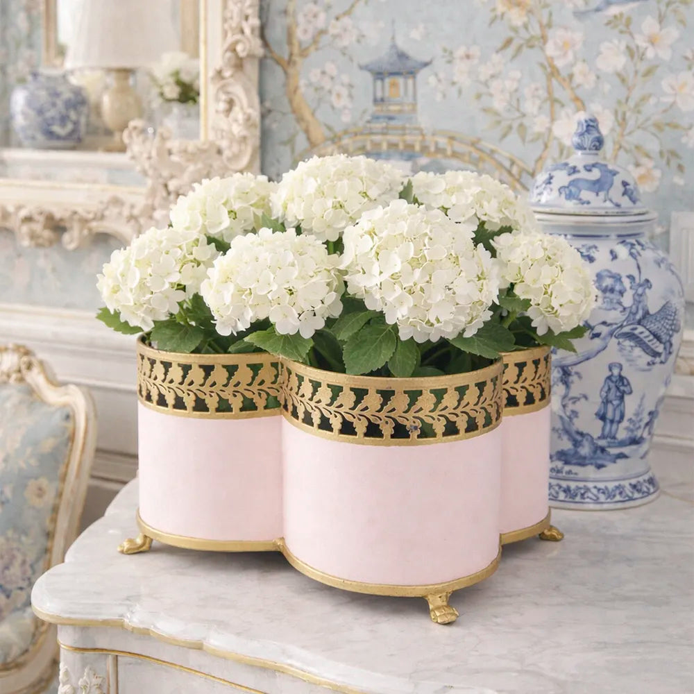 Decorative blush pink quatrefoil planter with white hydrangea flowers on a table in an elegant room.