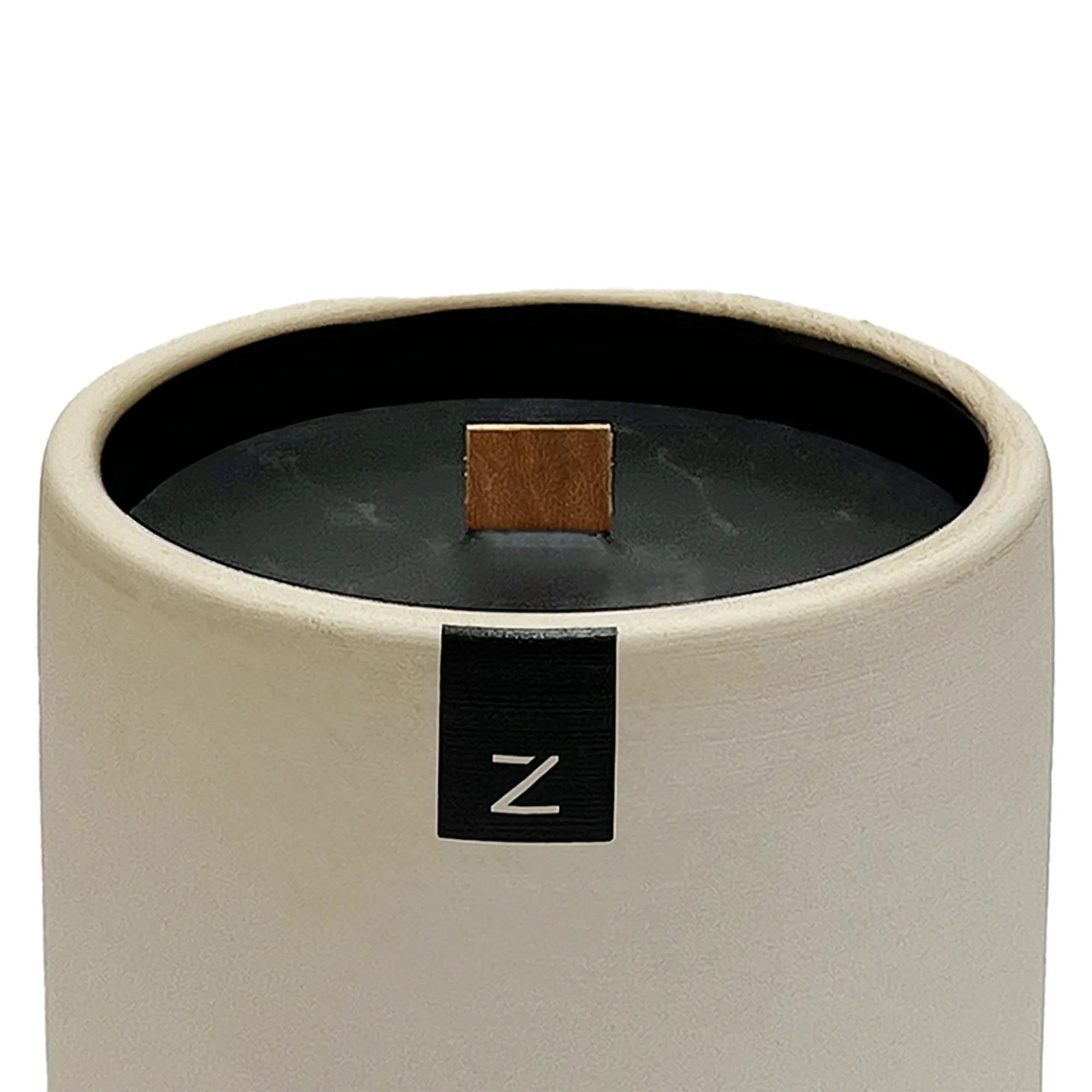 Close up of a ceramic candle holder with a black interior and beige exterior, featuring a brand label with 'Z' on a white background.