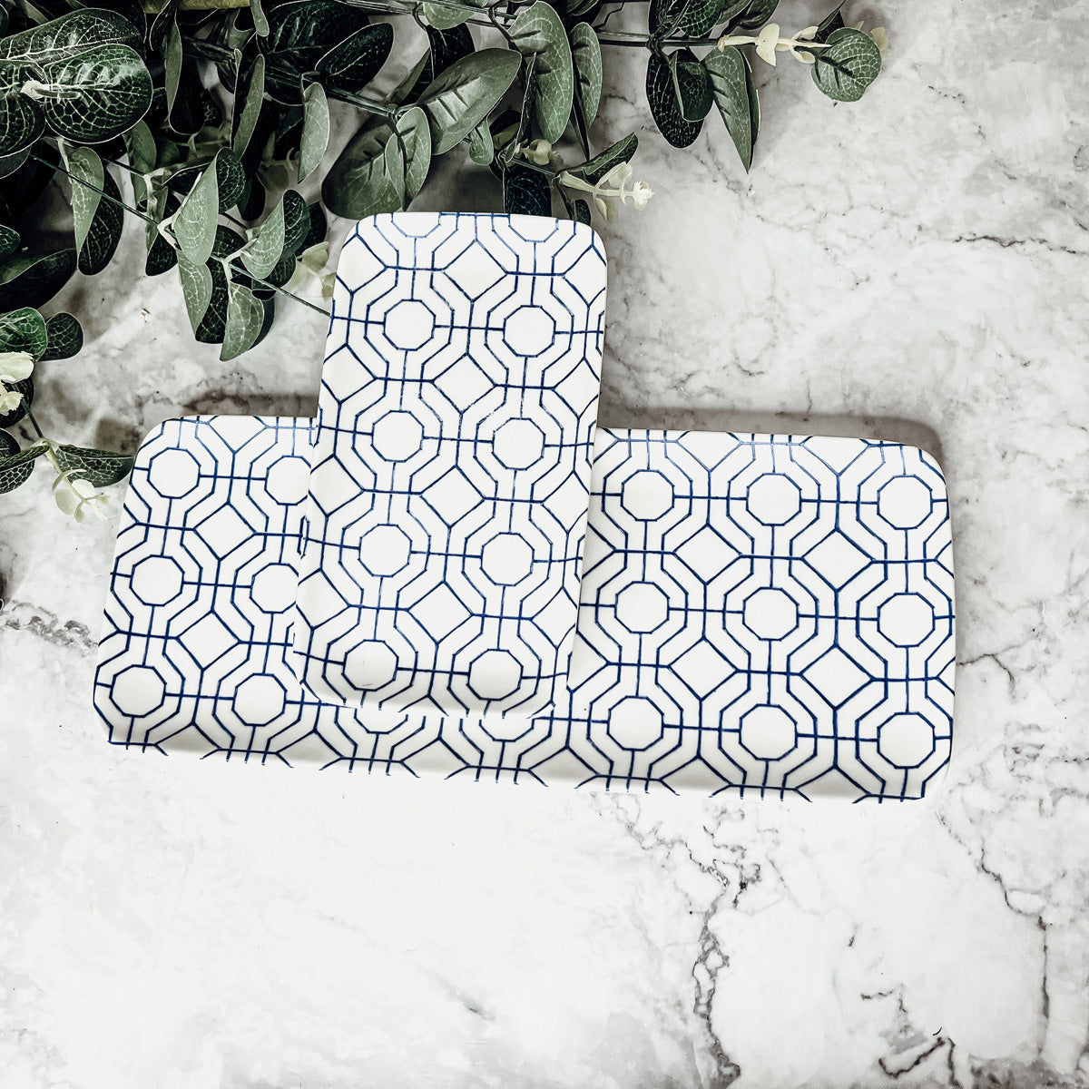 Two geometric blue and white serving trays on a marble surface with greenery