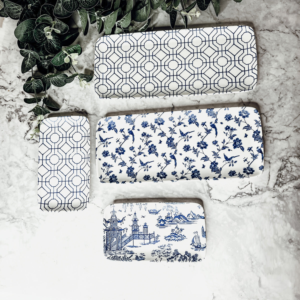 Set of four decorative serving trays with blue and white patterns on a marble surface.