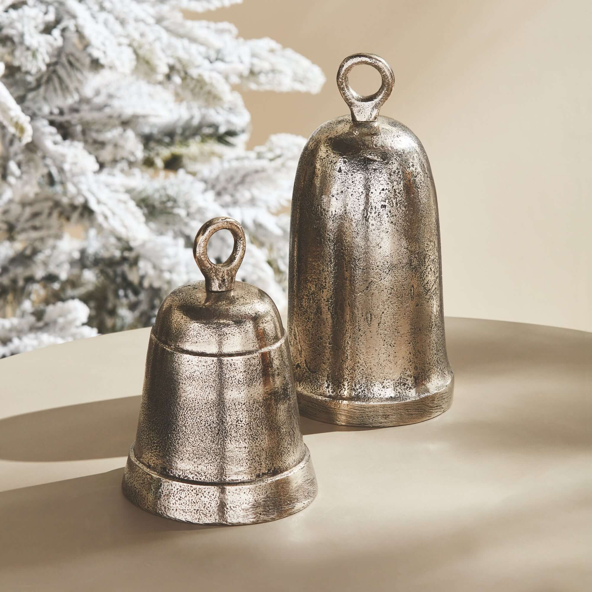 Two metallic bells on a beige surface with a blurred Christmas tree in the background