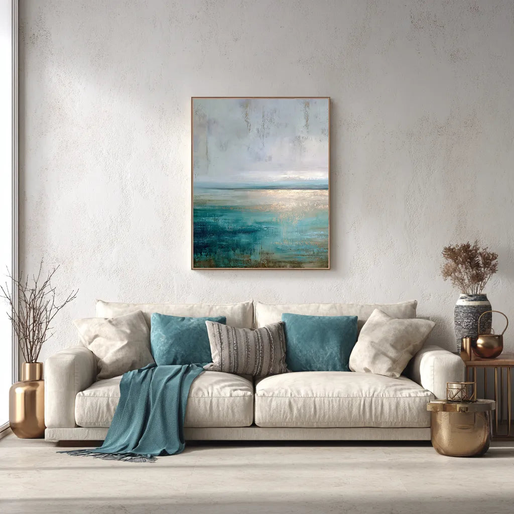 Elegant living room with teal abstract horizon canvas in walnut floating frame above a beige sofa with teal pillows and throw blanket, modern coastal wall art décor