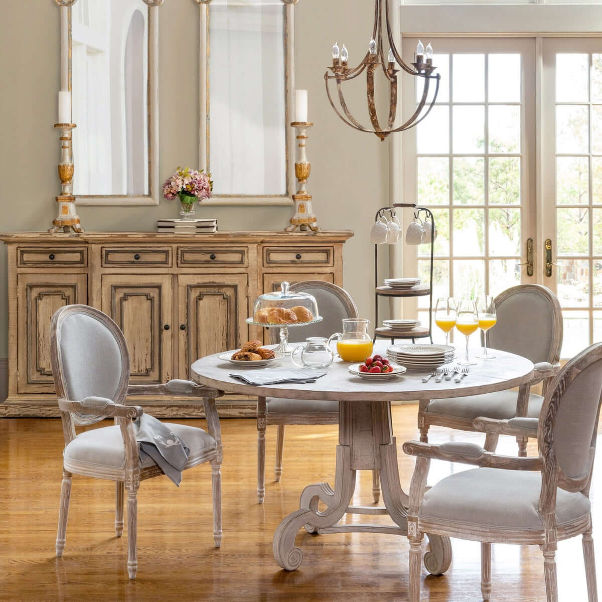 Dining room with a round table set for breakfast, wooden sideboard, and large mirror.