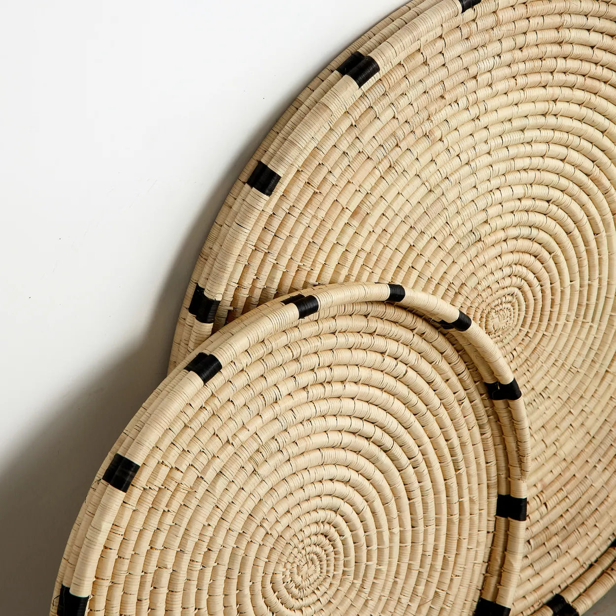 Two woven circular trays with black accents on a white background
