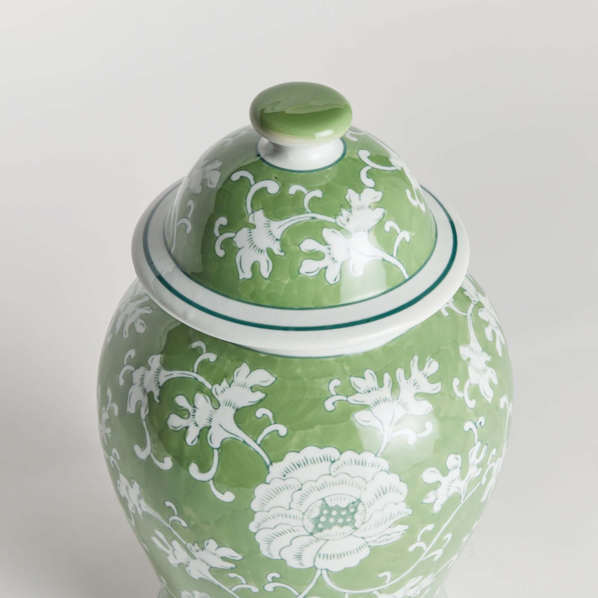 Green ceramic jar with white floral patterns on a light gray background