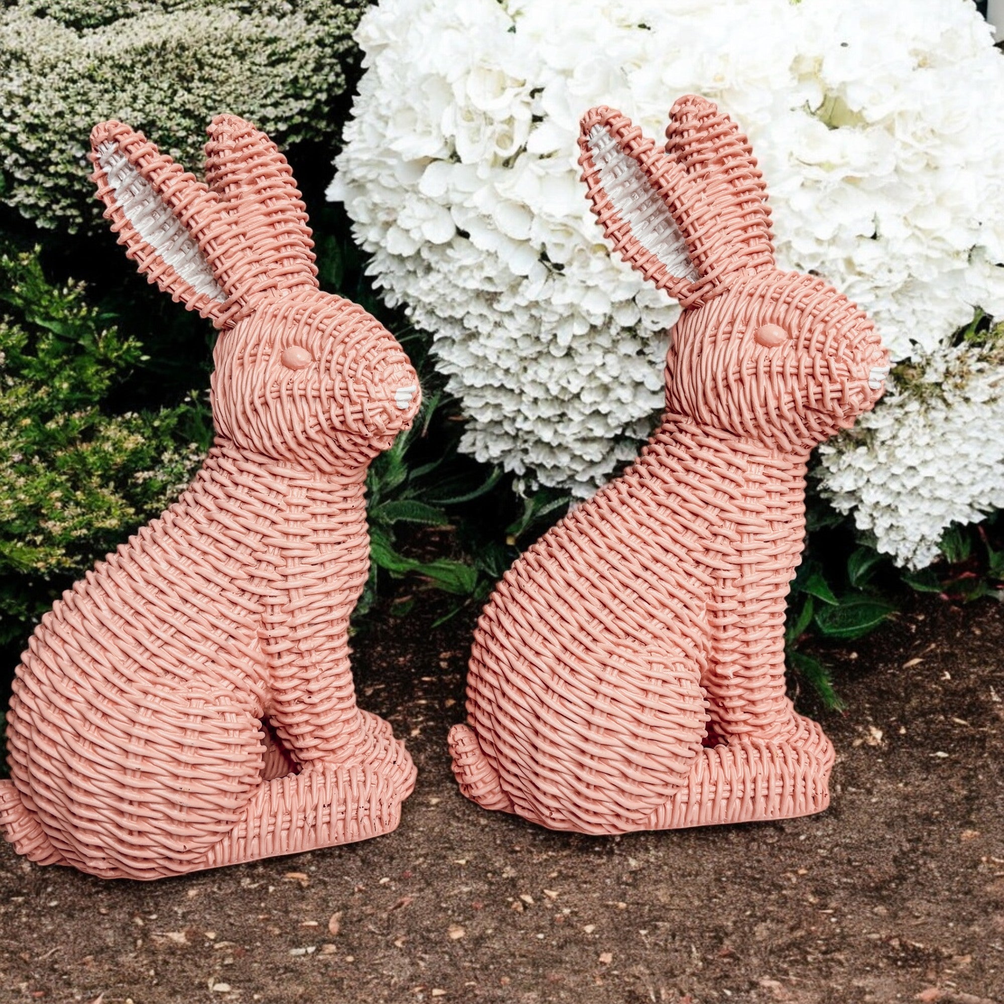 Two pink woven rabbit sculptures in front of white flowers and greenery.
