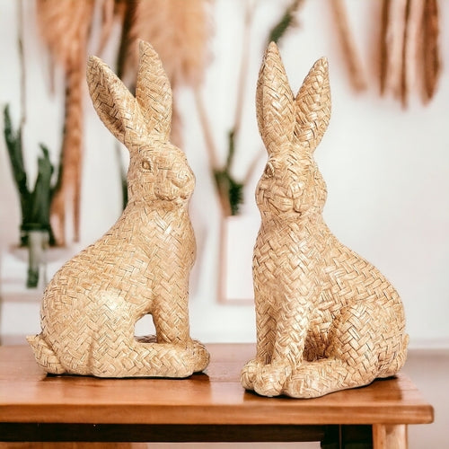 Two woven rabbit sculptures on a wooden surface with a blurred indoor background.