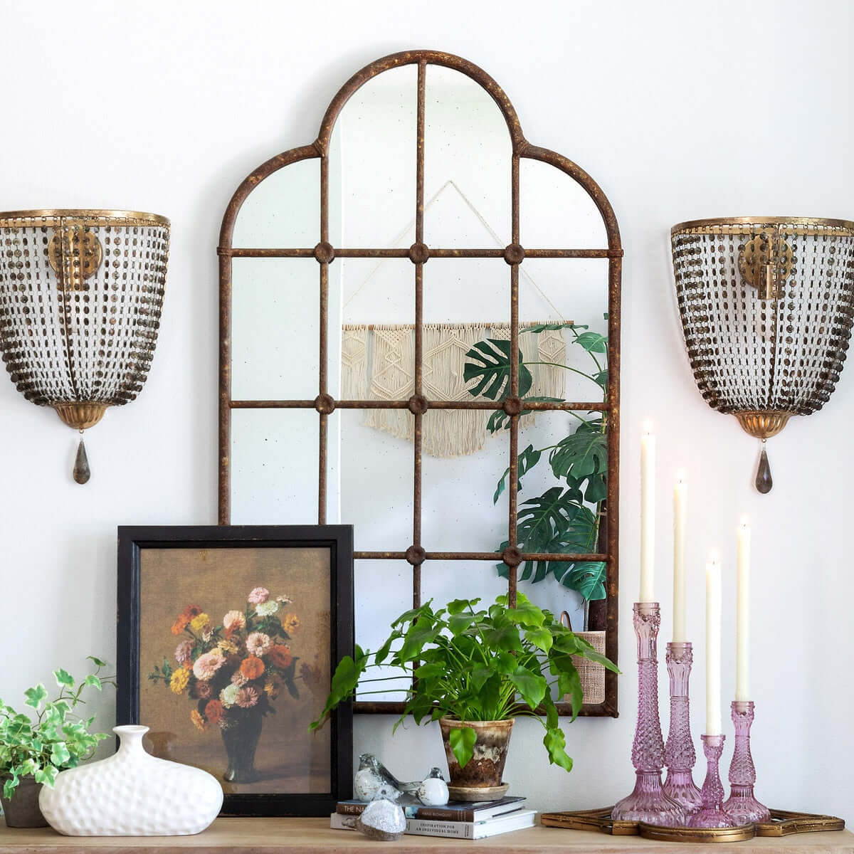 Decorative wall mirror with two wall sconces and a framed picture on a shelf.