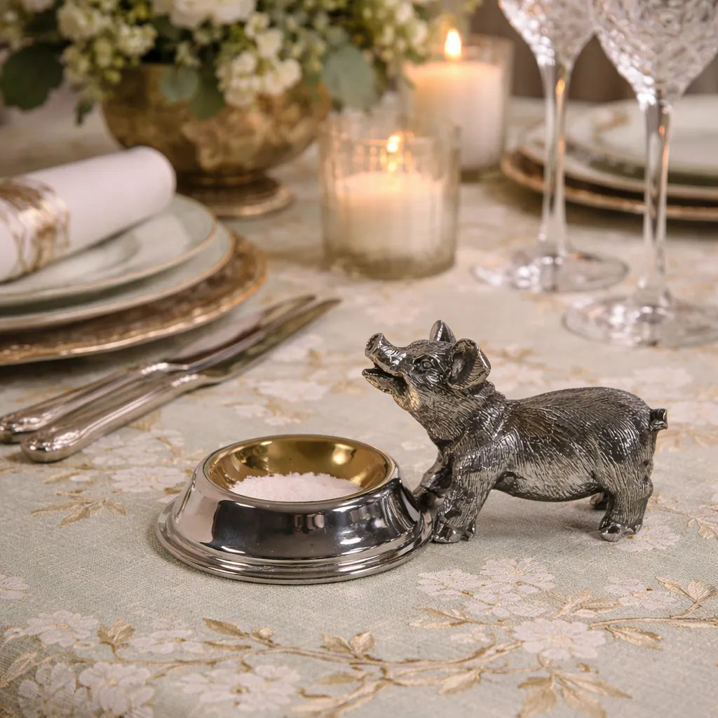 Decorative pig salt cellar on a table setting with candles and silverware.