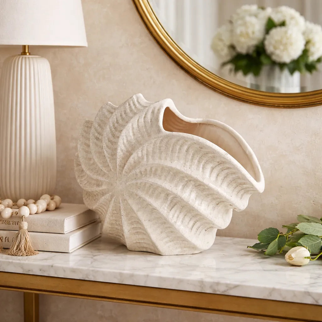Decorative shell-shaped vase on a marble surface with a lamp and mirror in the background.