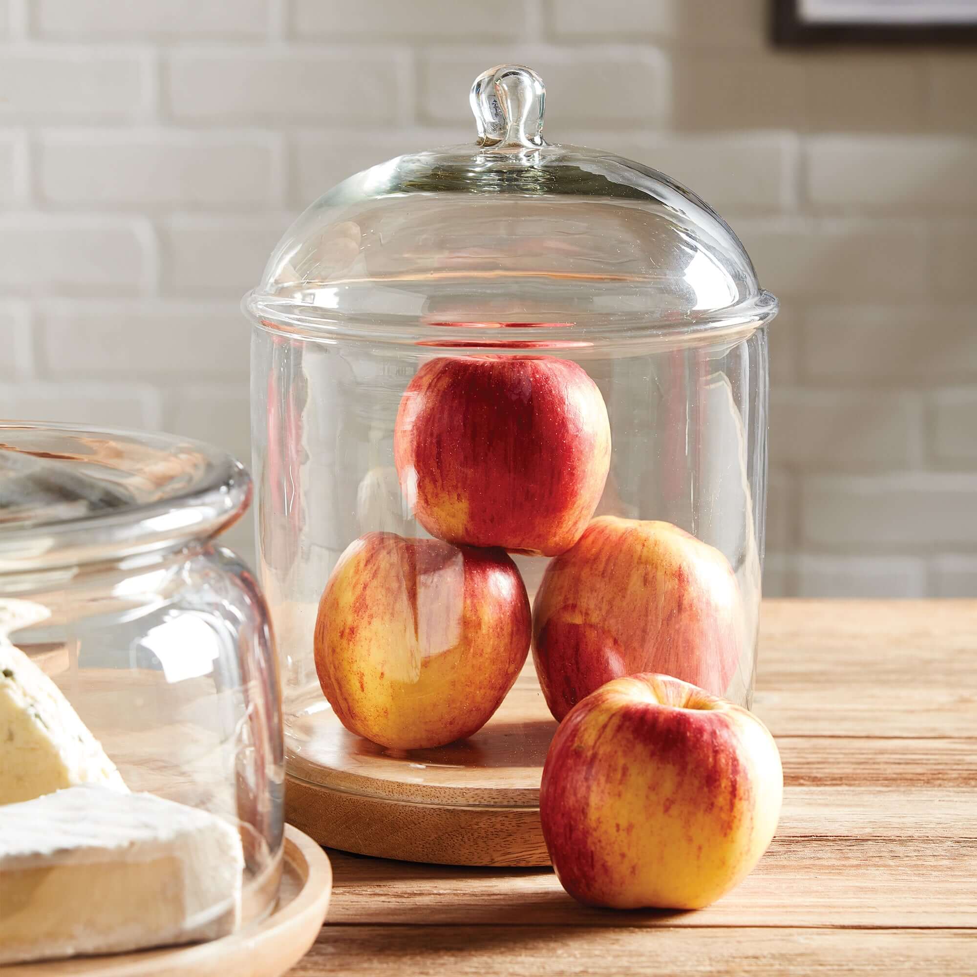 Glass cloche with a lid containing apples on a wooden surface.