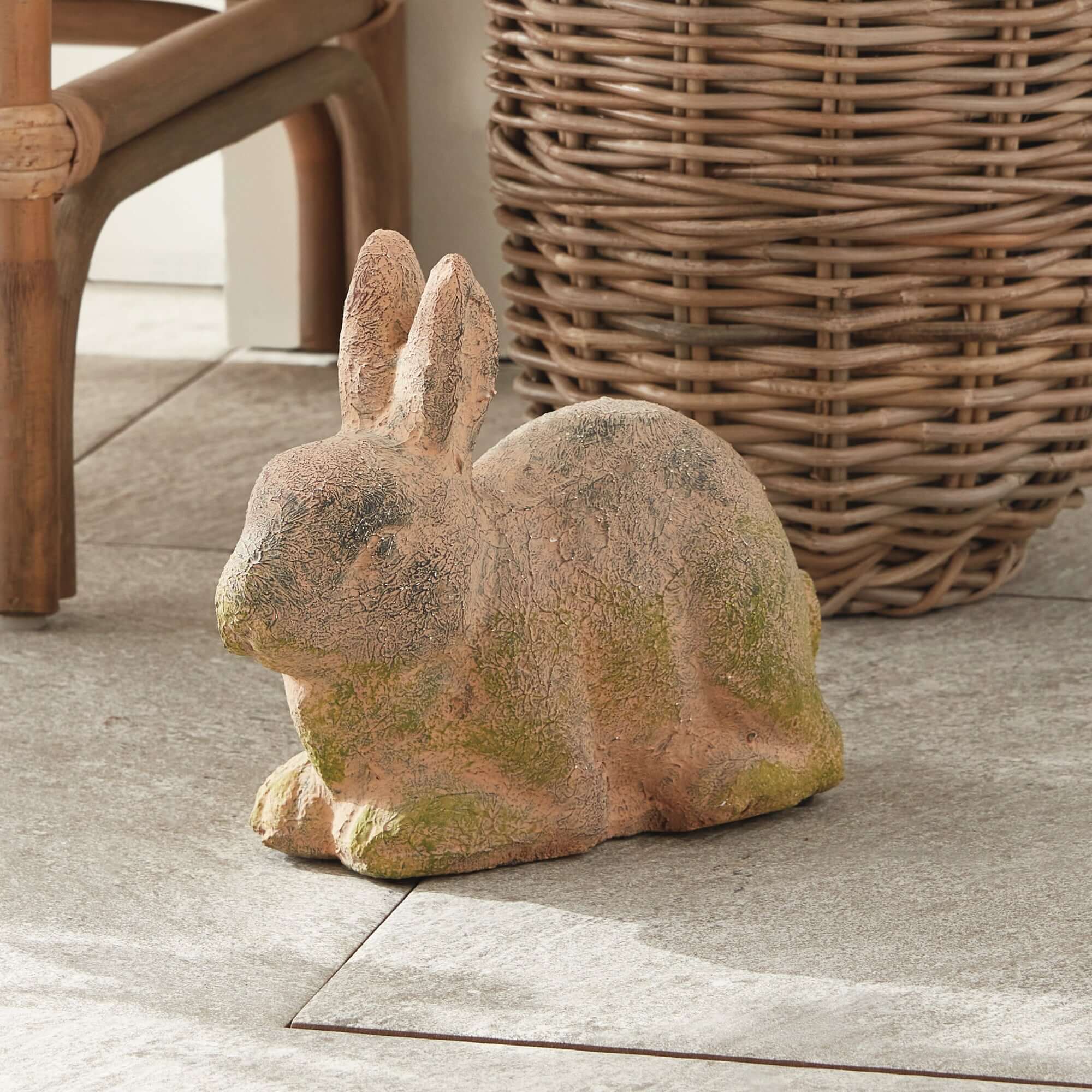 Stone rabbit sculpture on a concrete surface with wicker basket in the background